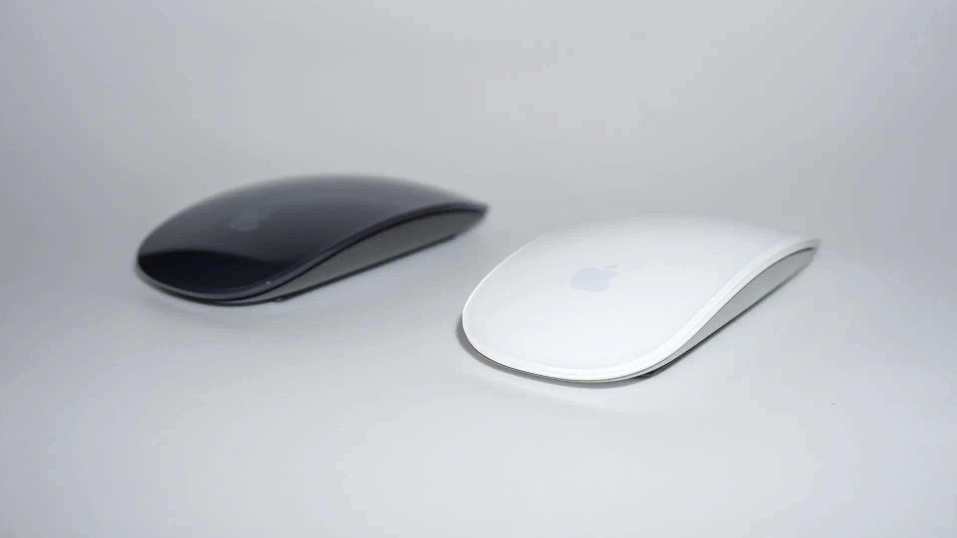 Two Apple Magic Mice side by side, one space grey and one white, on a plain background