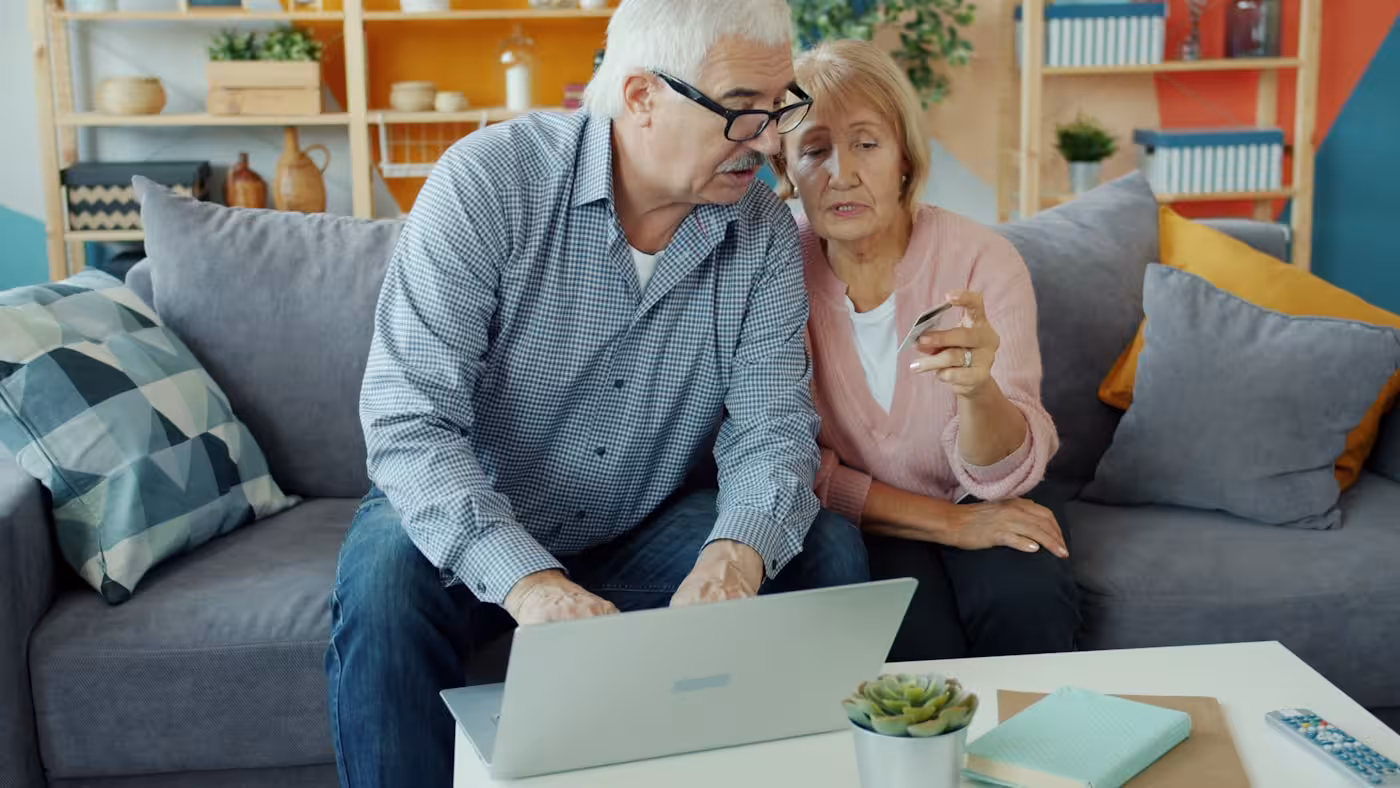 An older couple at a laptop holding a credit card — the kind of moment online scams target